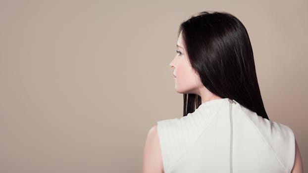 Profile view of a brunette woman in white attire indoors on a neutral background.